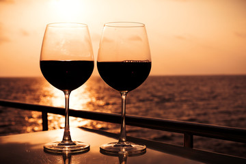 Glasses, red wine and tropical sunset with sea background, nobody.