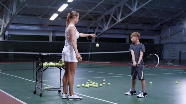 Beautiful woman tennis trainer teaching little boy how to play tennis