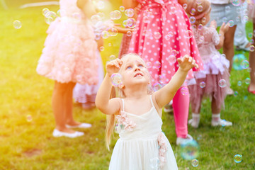 Little cute blond girl in a dress playing with soap bubbles duting children's party