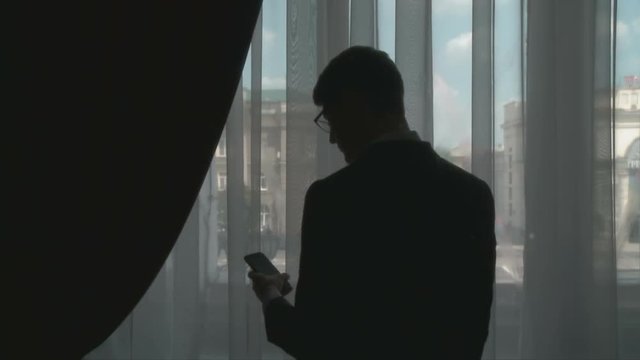 A young handsome man in a suit talking on a mobile phone near a large window indoors