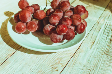 Fresh red grapes in a plate on wooden table, flatlay
