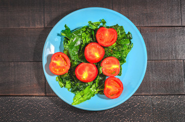 Tomatoes and greens spinach on a blue plate