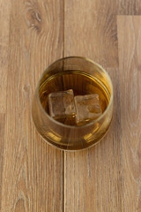 Glass of whiskey with ice on wooden background