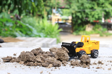 Truck toy car with sand and soil on the concrete floor with blur boken green environment  construction equipment at work ,construction concept, selective focus.