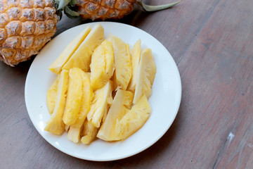 Cutting fresh pineapple and pineapple shelled Asian-style in white dish on the old wooden background. Tropical fruit concept.