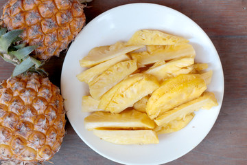 Cutting fresh pineapple and pineapple shelled Asian-style in white dish on the old wooden background. Tropical fruit concept.