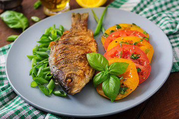 Fried fish carp and fresh vegetable salad on wooden background.