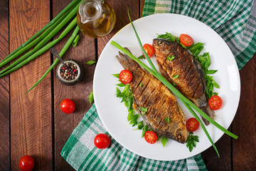 Fried fish carp and fresh vegetable salad on wooden background. Flat lay. Top view