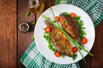 Fried fish carp and fresh vegetable salad on wooden background. Flat lay. Top view