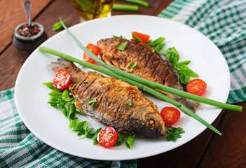 Fried fish carp and fresh vegetable salad on wooden background.