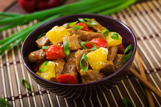 Veal fillet - stir fry with oranges and paprika in sweet and sour sauce on a wooden background.