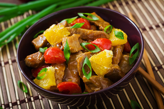 Veal fillet - stir fry with oranges and paprika in sweet and sour sauce on a wooden background.