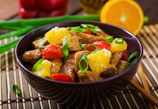 Veal fillet - stir fry with oranges and paprika in sweet and sour sauce on a wooden background.