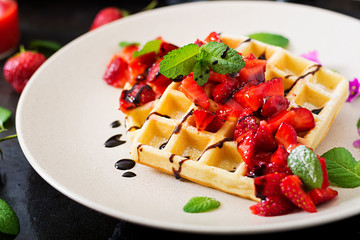 Belgium wafers with strawberries, chocolate and syrup on a plate.