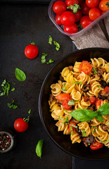Pasta Fusilli  with tomatoes, beef and basil in black bowl on table. Top view. Flat lay