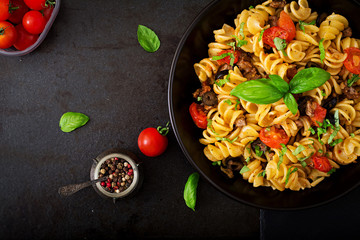 Pasta Fusilli  with tomatoes, beef and basil in black bowl on table. Top view. Flat lay