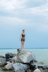 Girl practicing yoga on the rocks against the blue sky and the azure sea. Relaxation and Stretching. Young slim sporty woman do yoga outdoors.
