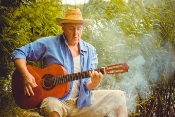 A mature European man in hat sing song playing guitar and have a good mood on a vacation near ...