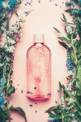 Natural Cosmetic product bottle on pink pale background with plant and flowers, top view, copy...