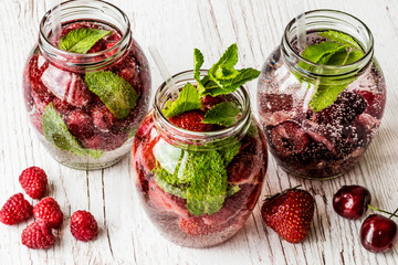 detox water with raspberry, strawberry, cherry on white wooden background. Healthy drinks