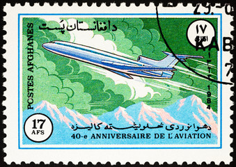 Passenger airliner over mountains on postage stamp