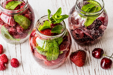 detox water with raspberry, strawberry, cherry on white wooden background. Healthy drinks