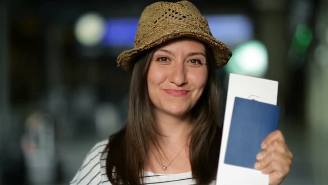 Closeup Portrait of Attractive Smiling Brunette in Summer Hat Waiting for Her Airplane at the Airport with Ticket and Passport in the Hands.