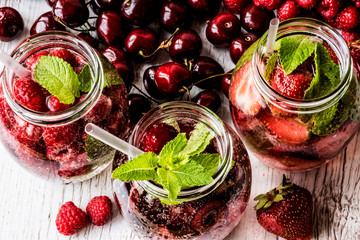 detox water with raspberry, strawberry, cherry on white wooden background. Healthy drinks