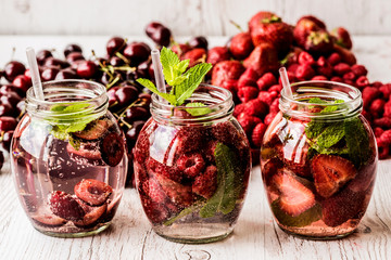 detox water with raspberry, strawberry, cherry on white wooden background. Healthy drinks