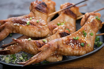 Close-up of bbq chicken wings on skewers served with sesame seeds and green onion, selective focus