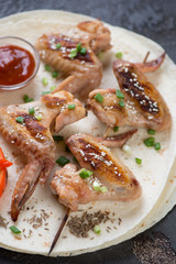 Close-up of barbecued chicken wings on skewers served on tortillas, selective focus, studio shot