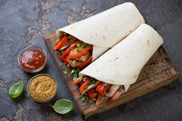 Wooden serving board with tortillas stuffed with chicken and vegetables, studio shot