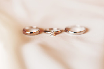 Set of three golden rings on silk textile - engagement ring with diamond and pair of wedding rings. Symbol of love and marriage.