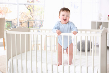 Cute little baby standing in crib at home