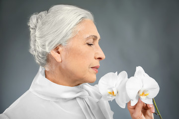 Beautiful elegant elderly woman with orchid flowers on gray background