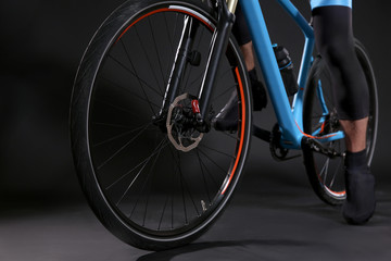 Fototapeta na wymiar Legs of young sporty cyclist riding bicycle on dark background