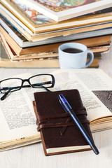 Fototapeta premium leather notebook with pen, glasses and coffee on a background of books