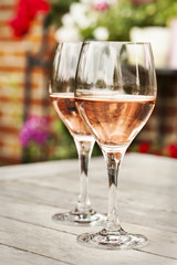 Two glasses of rose wine on wooden table with flowers on background
