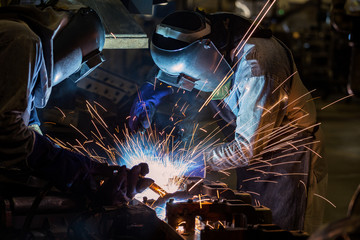 Industrial workers with protective mask are welding automotive part