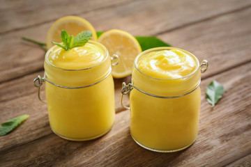 Glass jars with yummy lemon curd on wooden table