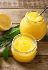 Glass jars with yummy lemon curd on wooden table