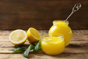 Glass jars with yummy lemon curd on wooden table
