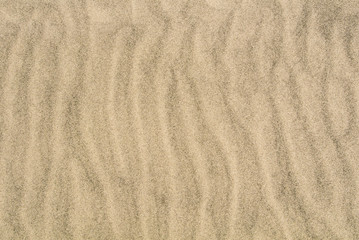 Fototapeta na wymiar A sand texture, close-up macro view to a sand of a beach with shapes, waves and lines formed by the blow of the wind.