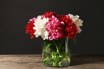 Vase with beautiful peonies on wooden table against dark background