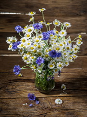 Bouquet of chamomiles and cornflowers in the vase on the wooden table.