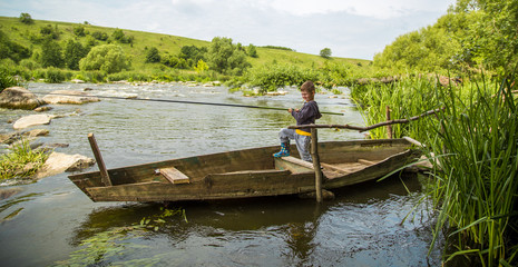 Fototapeta na wymiar Boy with fishing rod fishing in a wooden boat