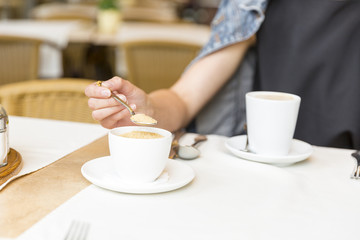 Beautiful young girl resting in a cafe, adding sugar into coffee