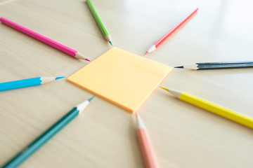 Many different colored pencils put around post it on wooden background
