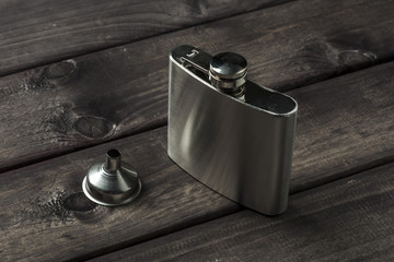 Metall hip flask with cup on wooden backdrop