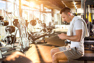 Young muscular man using mobile phone at the gym.